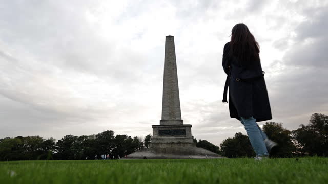 A sad woman walks hopelessly, Wellington Monument, Wellington Monument in Phoenix Park in Dublin Ireland, famous tourist attraction in Ireland, landscaped park in Europe, famous city parks in Europe