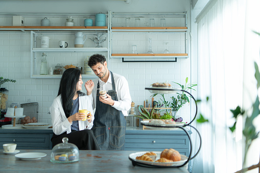 A husband wears an apron while cooking dinner with his wife. The duo took a break to sip coffee and sample the completed bread.