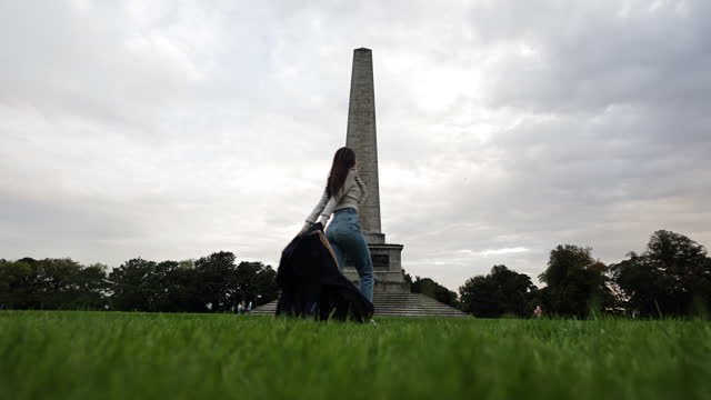 Young woman running happily drops her clothes on the ground, Wellington Monument, Wellington Monument in Phoenix Park in Dublin Ireland, famous tourist attraction in Ireland, landscaped park in Europe, famous city parks in Europe