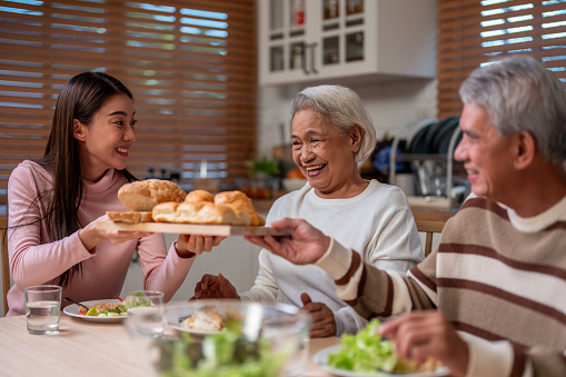 Asian lovely family having lunch, enjoy eating party in house together. Attractive senior elderly grandparent and young beautiful daughter eat foods celebrate weekend reunion at dining table at home.