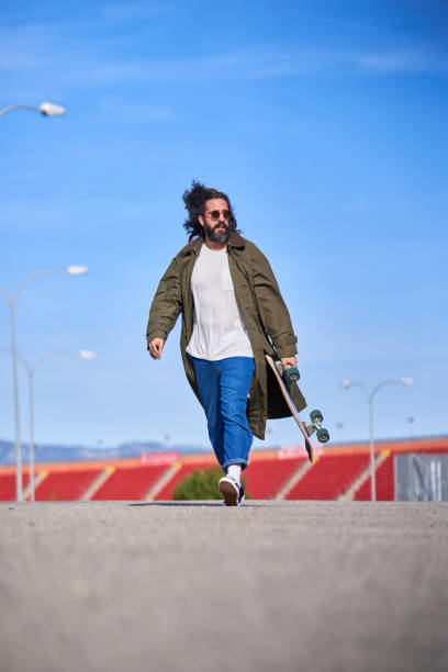 istock Stylish man walking with longboard on stadium 2067647231