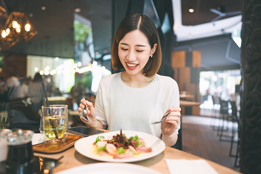 Weekend city break people lifestyle concept. Young adult asian woman eating healthy food diet meal. At indoors cafe restaurant on day. Happy smile face and short hair person.