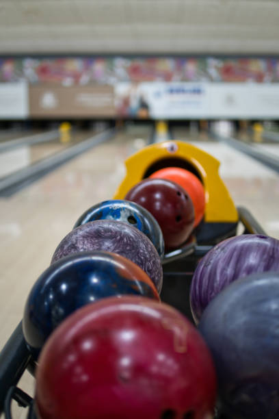 Colorful bowling balls in return machine at bowling alley. Lanes and pins in blurred background.