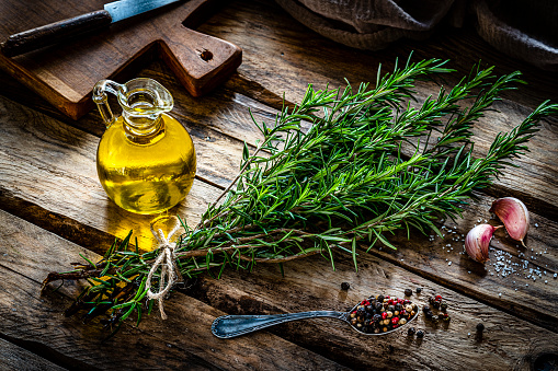 Bottles of essential oil with basil leafs in bowl on gray wooden table