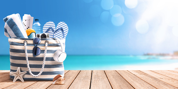 Beach bag with accessories on the beach boardwalk at the tropical resort, ocean in the background, travel and summer vacations concept