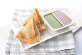 deep fried indian curry potato vegetable samosa snack with green mint yogurt sauce on white background vegan appetiser dim sum snack Halal food restaurant cuisine menu for cafe
