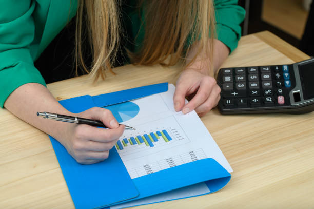 A woman at a desk opens a folder with financial data next to a calculator