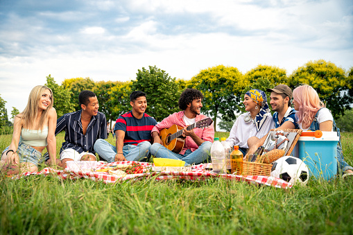 Group of multiethnic teenagers spending time outdoor on a picnic at the park. Concept about generation z, lifestyle and friendship