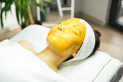 Young woman with a golden mask applied to her face in the beauty center. beauty concept