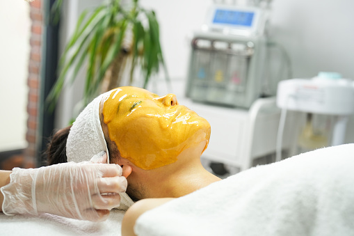 Young woman with a golden mask applied to her face in the beauty center. beauty concept