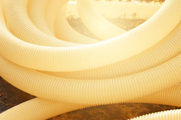 Perforated yellow drainage pipe with slots in a roll twisted in a spiral close up.