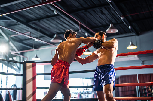 Healthy, fit and active male boxer training, exercising and sparring with his coach, trainer or instructor in the gym or health club. Man preparing for a boxing fight, match or competition
