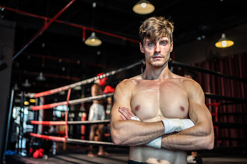 Portrait of Caucasian young sportsman exercising in dark fitness gym. Attractive male athlete looking at camera after workout to maintain strong muscle for health care in gym stadium or gymnasium.