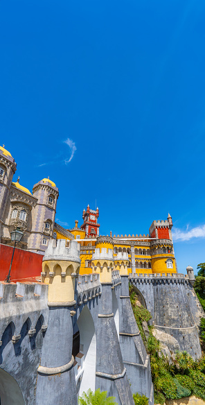 Exterior view of the Pena Palace with yellow, red colored walls and mosaics on the hill with the wall and fortified walls, under a sunny blue sky. Sintra. Portugal. Vertical banner. Copy Space.