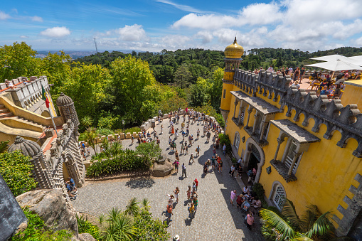 Aerial panoramic view of tourists visiting the Pena Palace and the restaurant terrace full of people having snacks and contemplating the leafy mountains of Sintra.