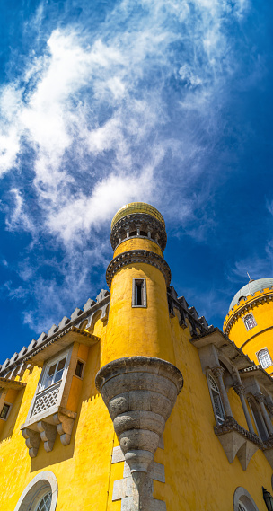 Low angle view of a battlement with a medieval window loophole and the upper part finished in columns with a dome of yellow mosaics from the Pena Palace. In Sintra under a sunny blue sky. Portugal.