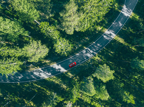 Aerial view of red car with a roof rack on a country road and green woods in Finland