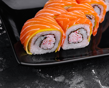 sushi rolls with salmon and crab on black plate
