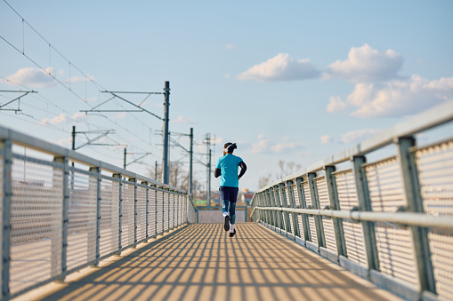 Back view of African American athletic man running over the bridge. Copy space.