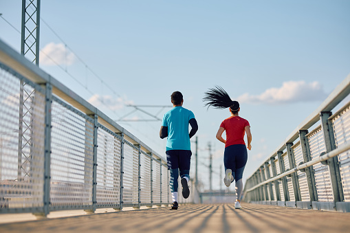 Rear view of couple of athletes jogging while exercising together outdoors. Copy space.