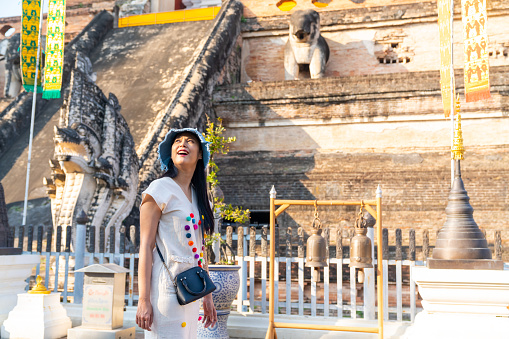 Happy Asian woman traveler enjoy and fun outdoor lifestyle travel in Thailand on summer holiday vacation. Attractive girl tourist travel old traditional Buddhist temple in Chiang Mai.