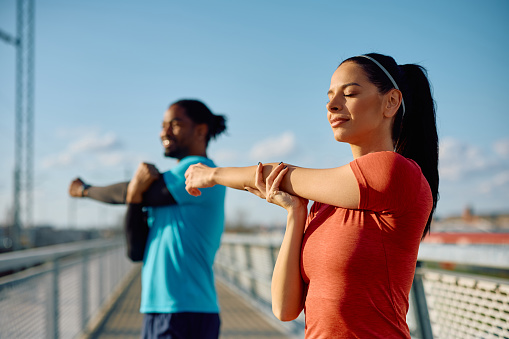 Athletic couple stretching their arms during sports training outdoors. Focus is on woman.