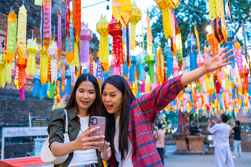 Asian woman friends using smartphone taking selfie or vlogging together during travel old Buddhist temple in Chiang Mai. Attractive girl enjoy outdoor lifestyle travel Thailand on summer vacation.
