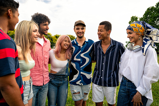 A large group of teens stand side-by-side at the top of a grassy hill as they pose together outside for a casual back-to-school portrait.  They are each dressed comfortably in fall layers and smiling.