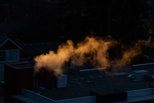 The photograph captures the golden hues of building exhaust illuminated by the soft light of dusk. The smoke rises from the top of the structure, creating a dynamic silhouette against the dim backdrop. The color of the exhaust stands in stark contrast to its surroundings, emphasizing the energy consumption and thermal activities in urban life.