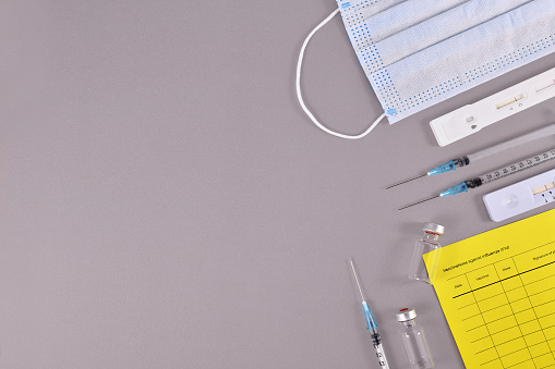 Virus antigen test, vaccine passport, medical face masks, vaccine vials with syringes on gray background with copy space