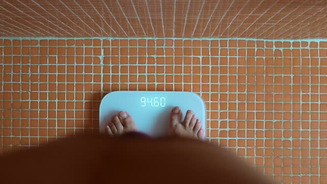 Male bare feet stepping on white digital scales. Man weighing himself at home: close-up, top view. Weight measurement, control, wellness and diet concept.