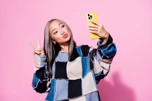 Photo of charming girl with dyed hair dressed pullover make selfie on smartphone show v-sign pouted lips isolated on pink color background.