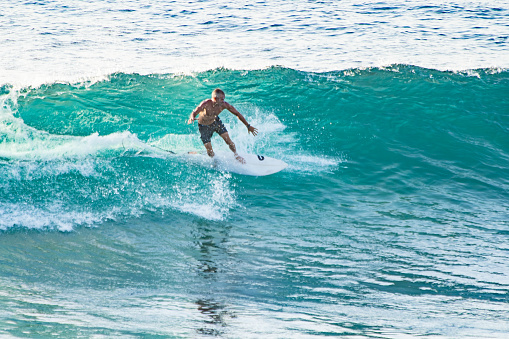 Bali, Uluwatu - A surfer, balanced on a surfboard, rides a turquoise wave. The clear blue ocean serves as a vibrant backdrop.