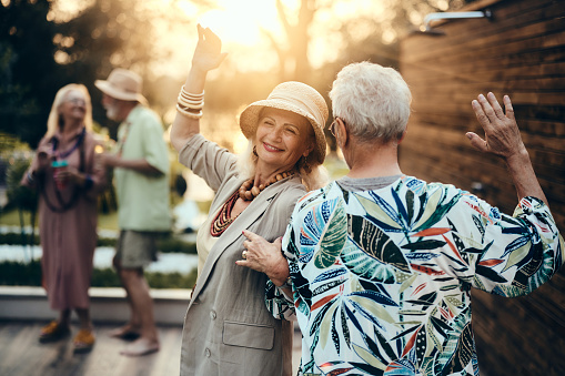 Happy mature couple having fun while spinning and dancing during a party in the backyard at sunset.