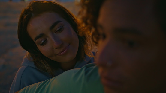 Enamoured girl face looking boyfriend at night beach close up. Relaxed lady listening serenade at evening nature. Tattooed musician hand playing guitar touching strings. Romantic couple enjoying music