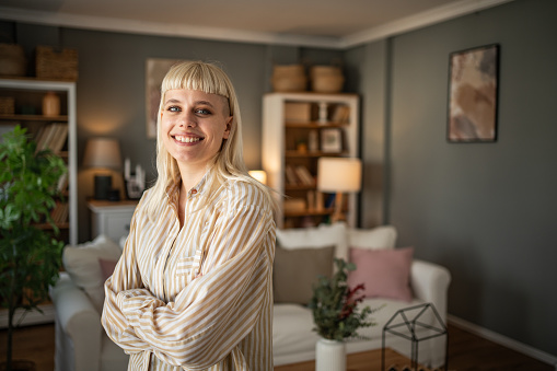 Portrait of a young woman with an interesting style standing in the living room of her home, she is confident and happy