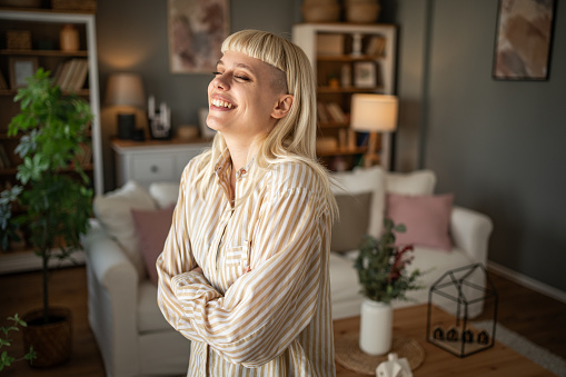 Portrait of a young woman with an interesting style standing in the living room of her home, she is confident and happy