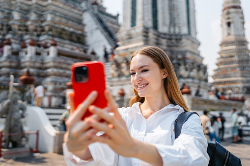 Young woman taking selfies at Wat Arun (The Temple of Dawn) in Bangkok in Thailand.
