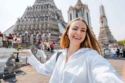 Young woman taking selfies at Wat Arun (The Temple of Dawn) in Bangkok in Thailand.