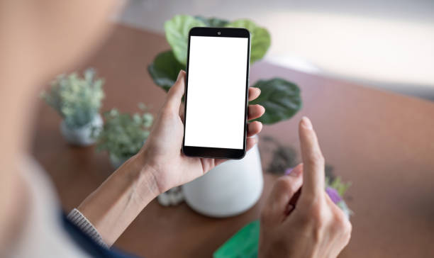 istock Simulated image of a blank white screen mobile phone Woman using mobile phone on table at home 2068006229