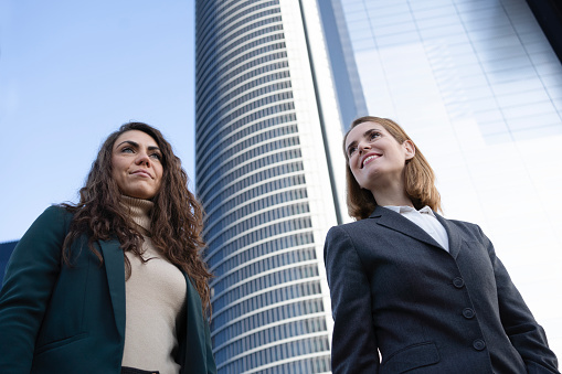 Low angle view of happy business females with a business tower behind. Women leadership concept.