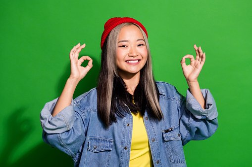Photo of positive toothy lady wear denim jacket smiling showing two okey signs isolated green color background.