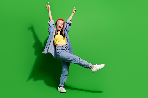 Full length photo of cheerful impressed lady wear denim jacket dancing disco walking empty space isolated green color background.