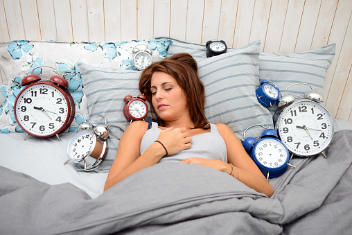 Woman in bed, many alarm clocks around her