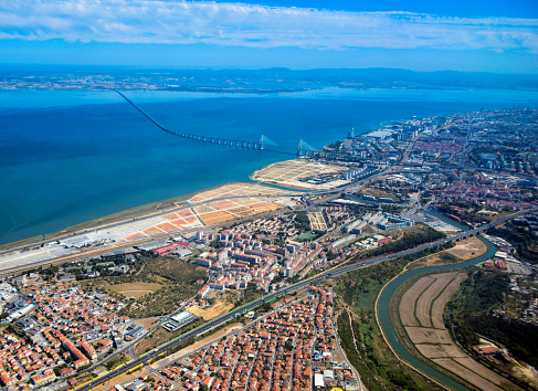 Lisbon, Portugal: aerial view of the Mar da Palha (Sea of Straw) inland sea in the Tagus River estuary, the eastern area of Lisbon and the Montijo / Alcochete on the southern bank, connected by the Vasco da Gama bridge. At the bottom the River Trancão can be seen, meandering towards its mouth, separating Bobadela from Sacavém, crossed by the A1 / E80 motorway. Above the bridge lie the Expo, Moscavide and Olivais areas. On the horizon is the south bank, with the Arrabida mountains and the Montijo Air Force base (BA6), on the top left. Shot from above São João da Talha.