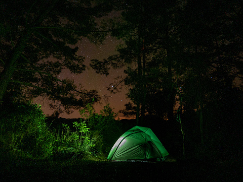 Bright green tourist tent at night in the forest with a starry sky