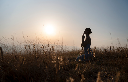 Side view of silhouette woman praying against sky during sunset