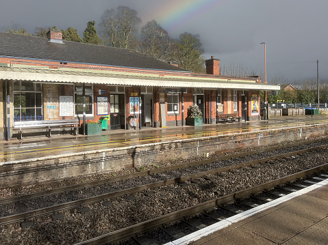 March 8th. 2024. A rainbow over Dorridge British Rail Network Rail commuter passenger diesel powered station West Midlands England UK. There are passengers on the platform on a sunny wet day.