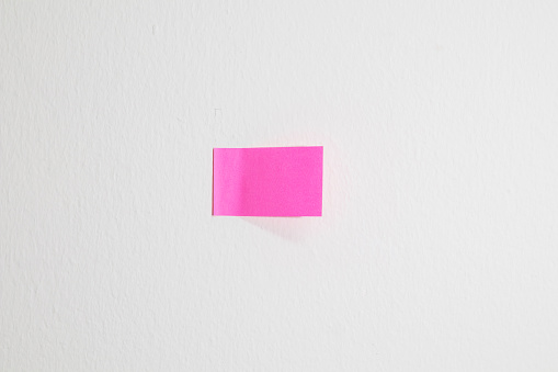 Pink paper note on a white wall background with empty space.