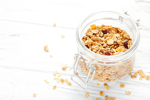 Tasty granola in glass jar on white wooden background